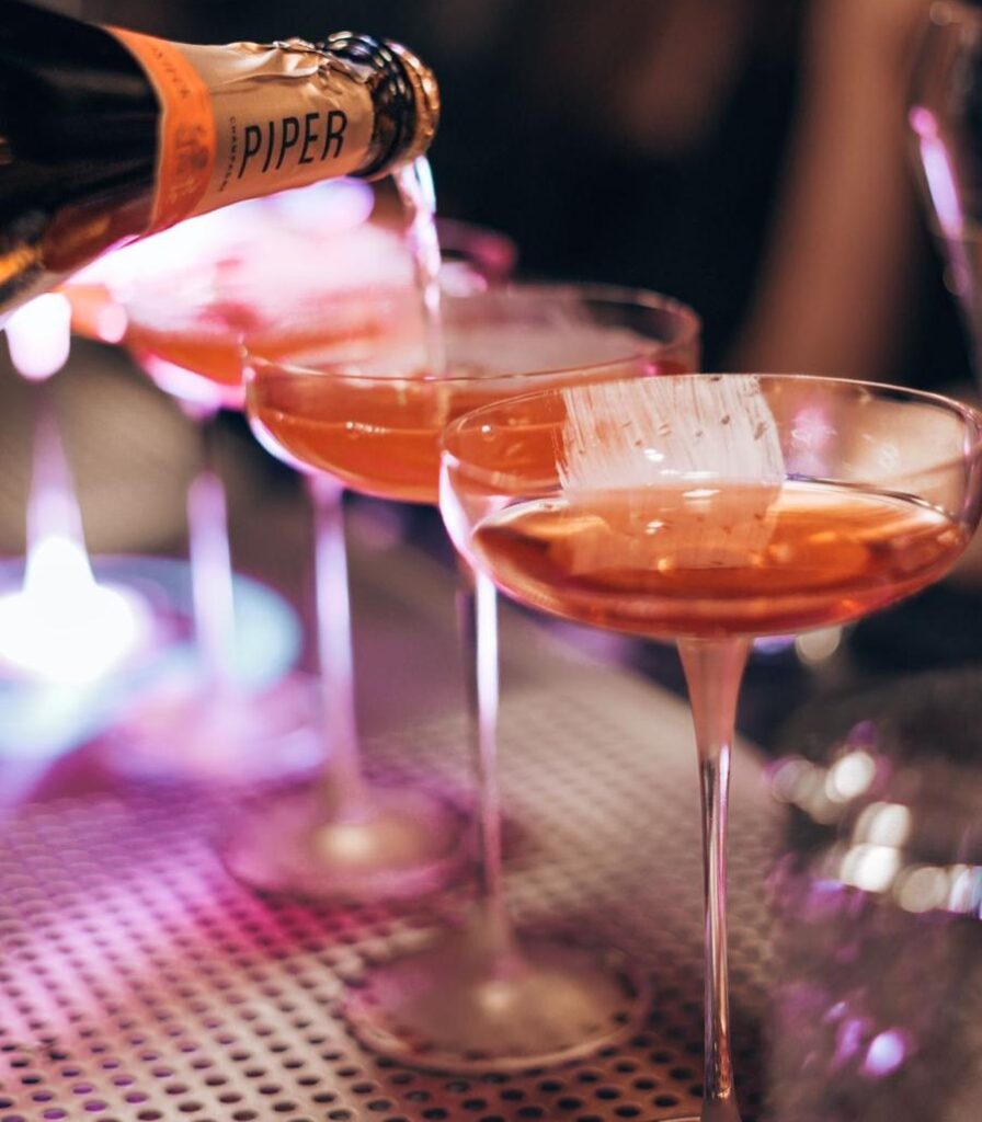 Drei Champagner Cocktails auf der Theke beim Einschenken mit Champagner Flasche