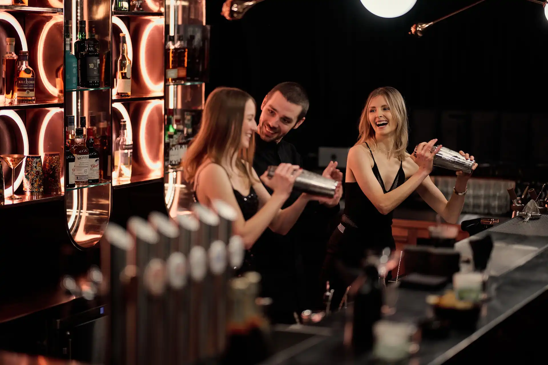 Frauen beim Cocktail Shaken gemeinsam mit Barkeeper hinter der Bar