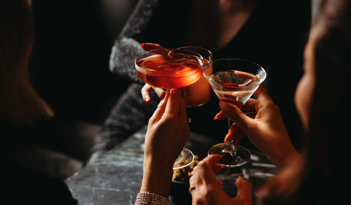 Vier Personen stoßen mit unterschiedlichen Cocktails in unterschiedlichen Gläsern an. Dabei sieht man nur die Hände
