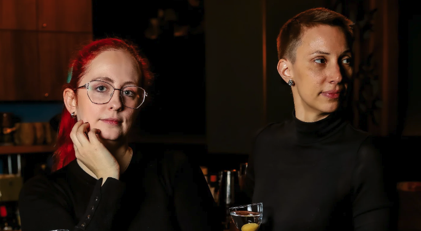 Die beiden Gastgeberinnen Laura und Sigrid stehen mit einem Martini in der Hand da, ganz in schwarz gekleidet.