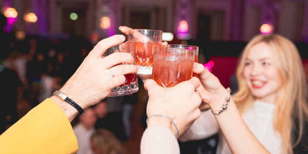 4 Menschen stoßen mit einem orangfarbenen Cocktail an