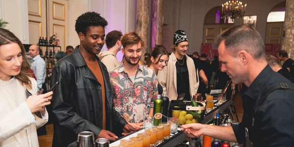 Junge Burschen stehen an einer Bar und warten wie der Barkeeper ihre Drinks fertig macht